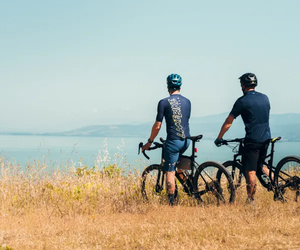 Two cyclists overlook a serene lake against a clear sky.